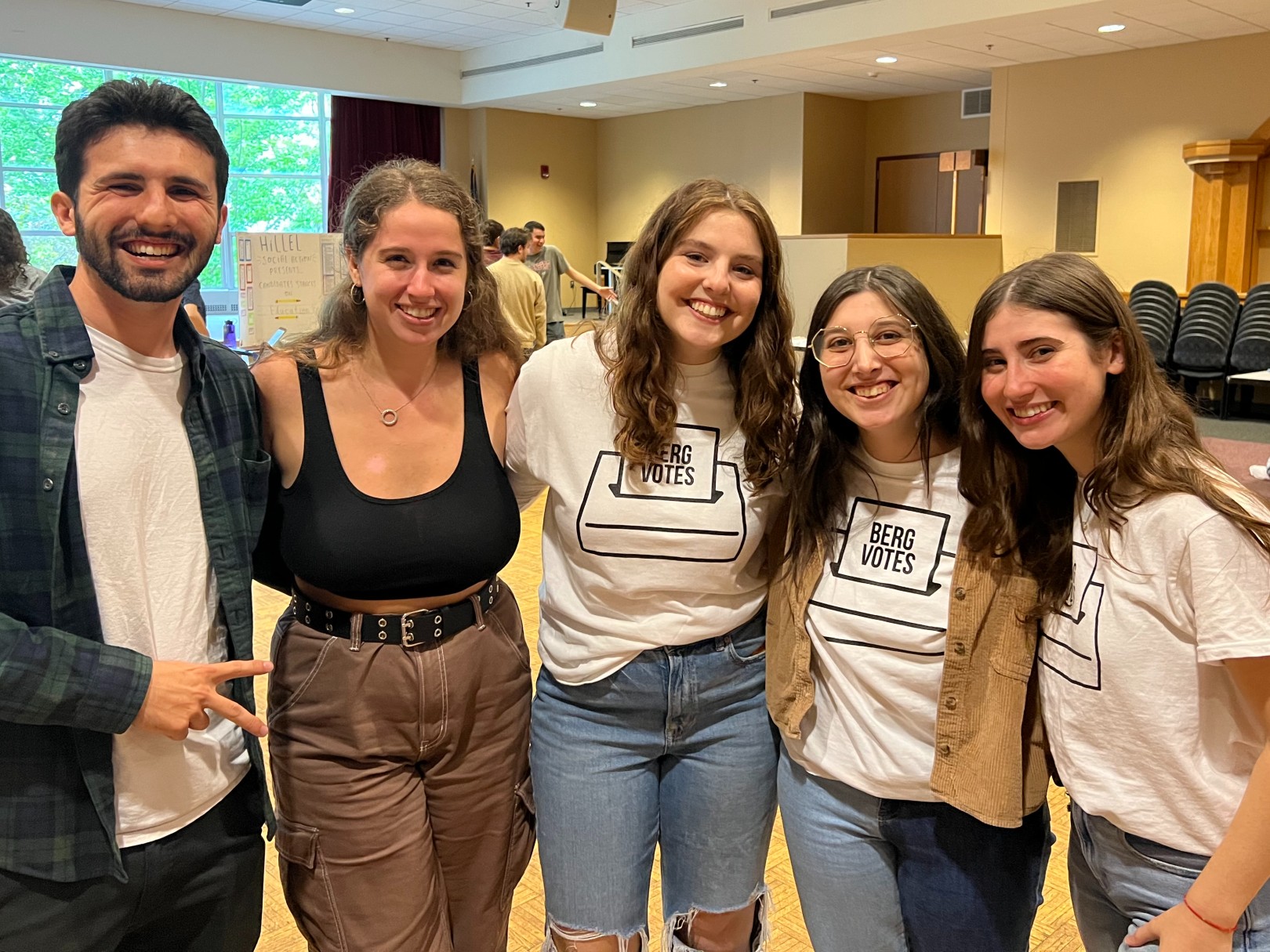 A group of five students stand, smiling, arms around one another.